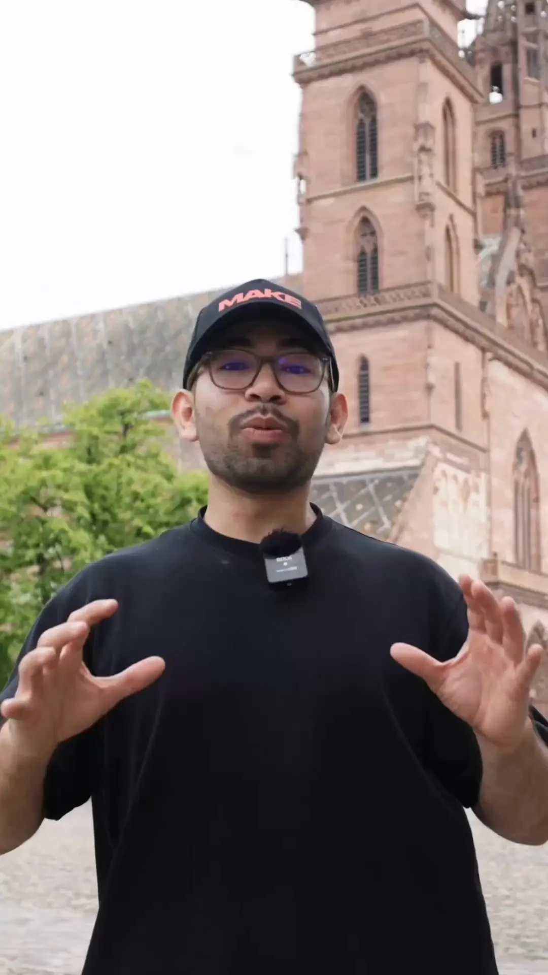Standbild aus der Video-Anzeige von MAKE: Sprecher mit MAKE-Kappe vor dem Basler Münster