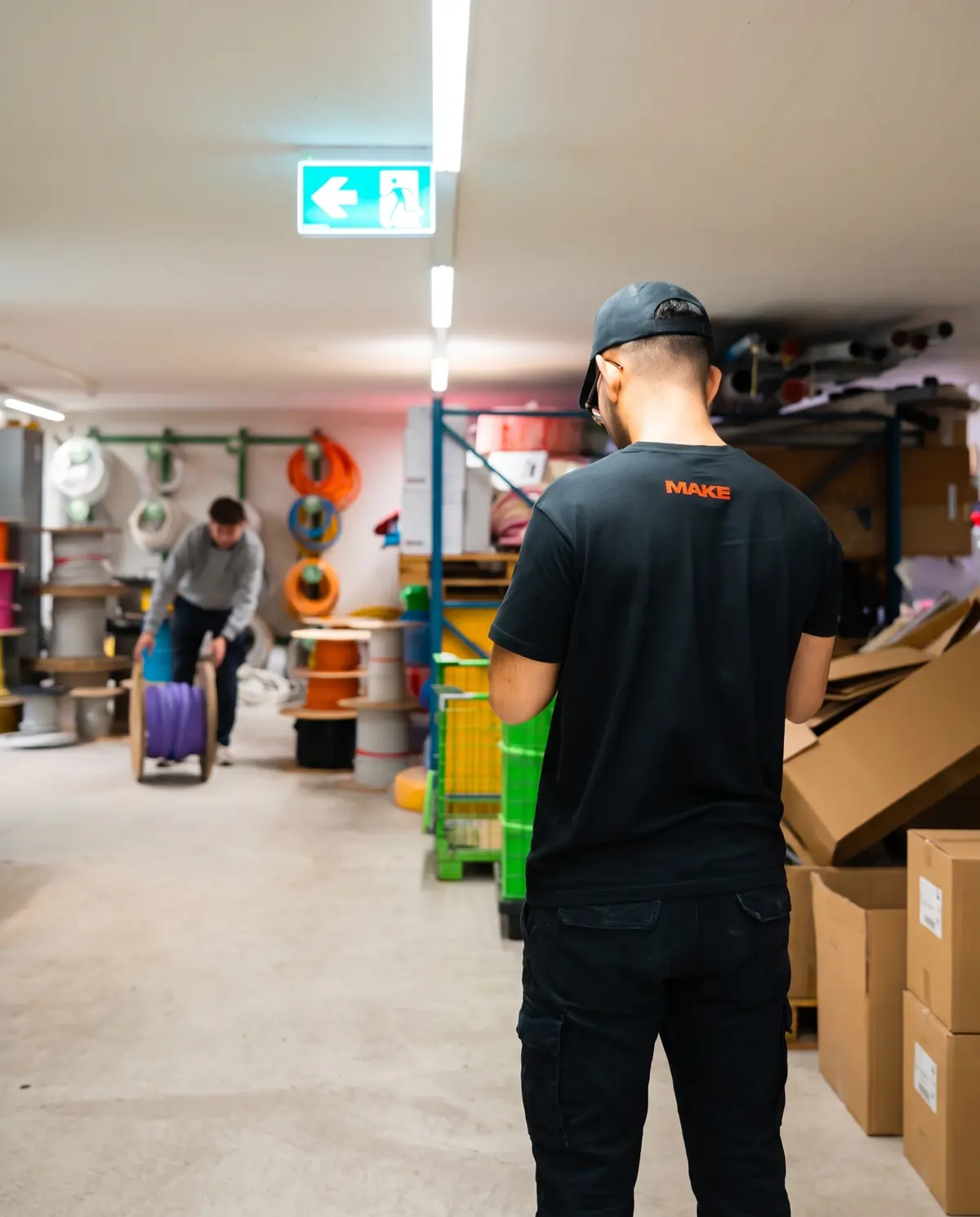 MAKE-Fotograf im Elektrolager eines Kunden, im Hintergrund rollt ein Mitarbeiter eine Kabeltrommel
