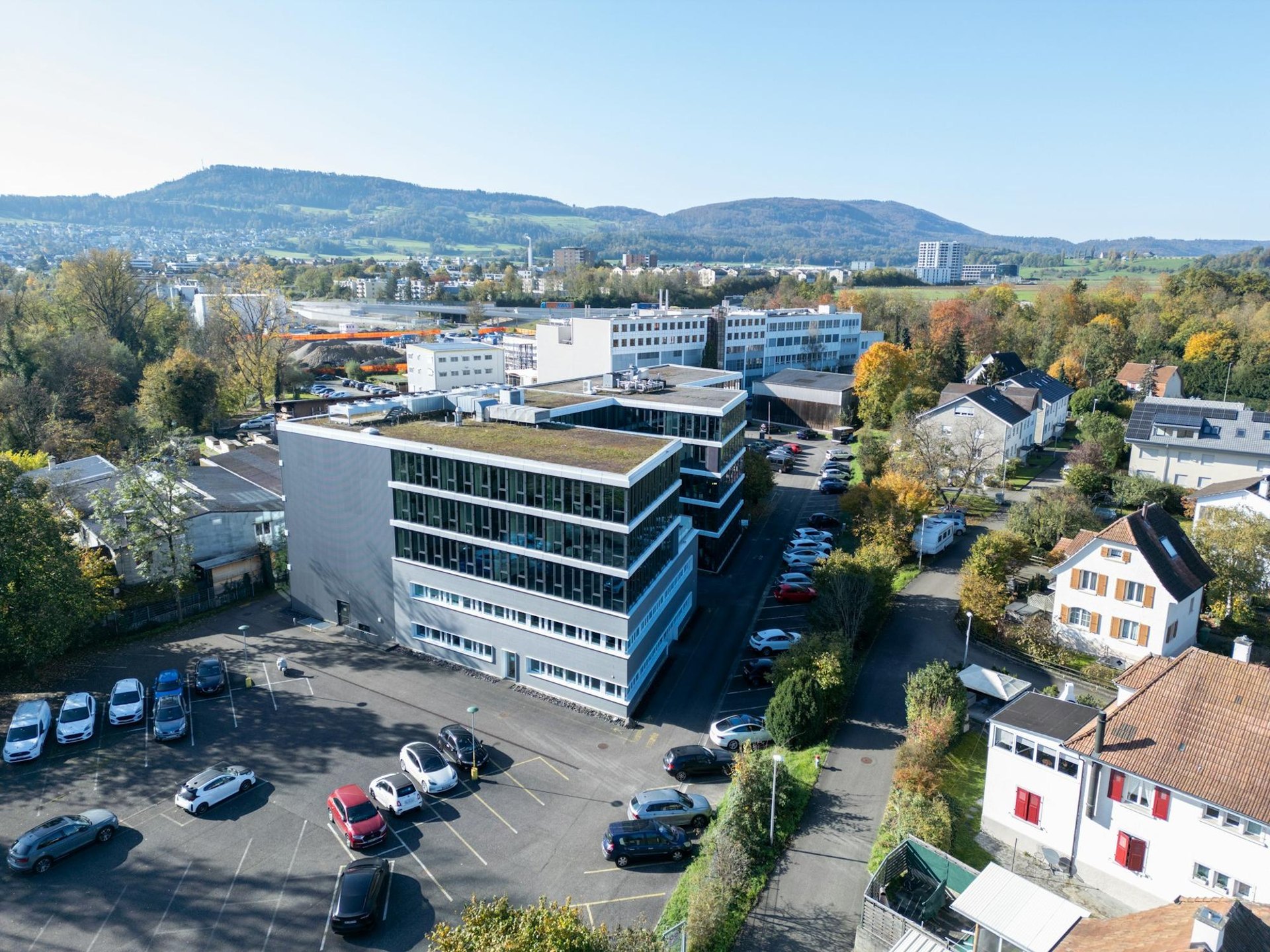 Ein modernes Bürogebäude mit Flachdach und vielen Fenstern, umgeben von Parkplätzen und Bäumen.