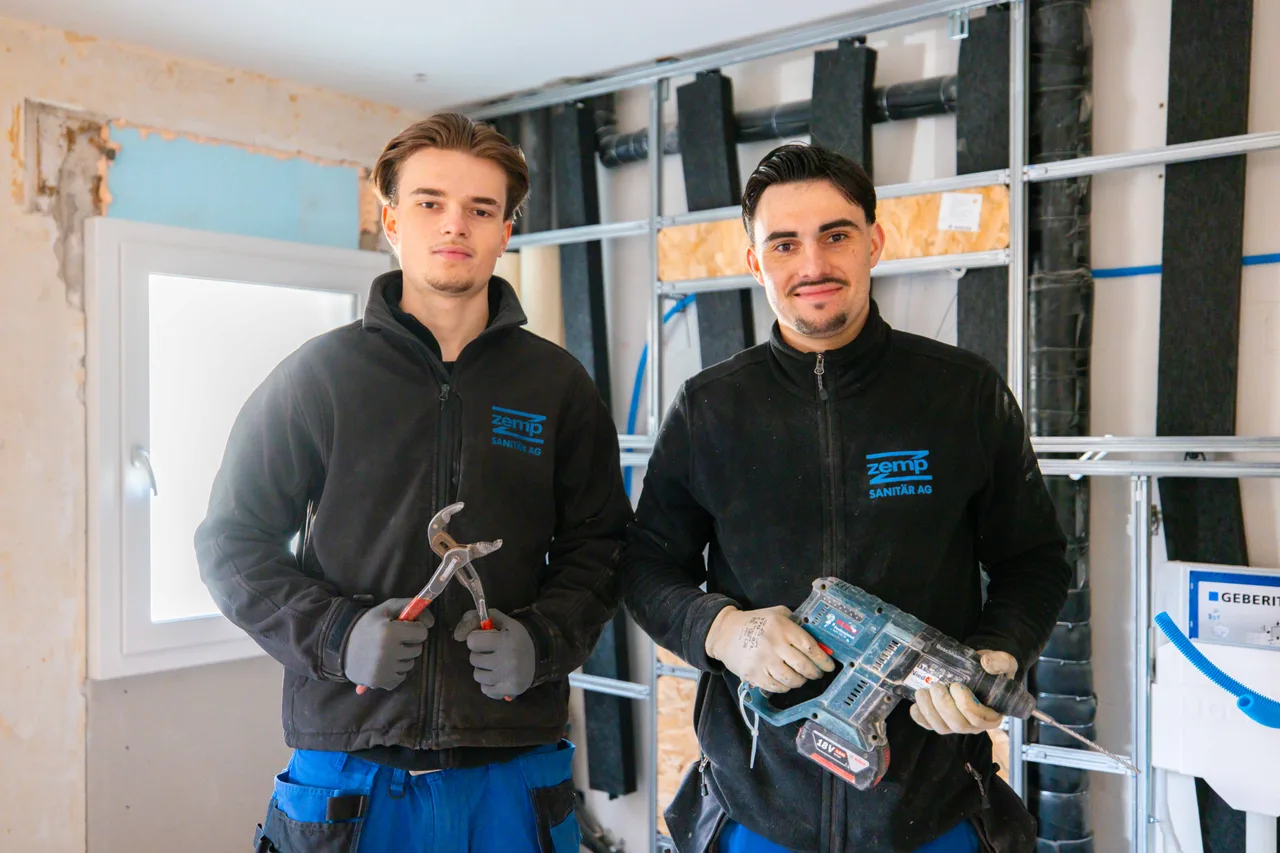 Zwei junge Monteure von Zemp Sanitär mit Zange und Akkuschrauber vor einer Vorwandinstallation im Rohbau