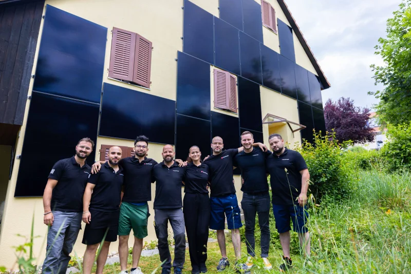 Mitarbeitende von AlpenEnergie vor einem Haus mit Solarmodulen an der Fassade
