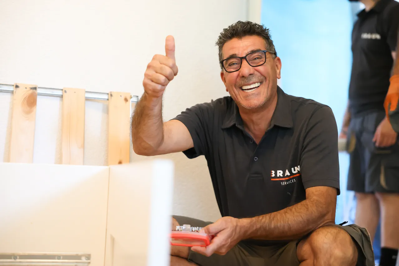 Mitarbeiter mit Brille lacht mit Daumen hoch bei der Möbelmontage