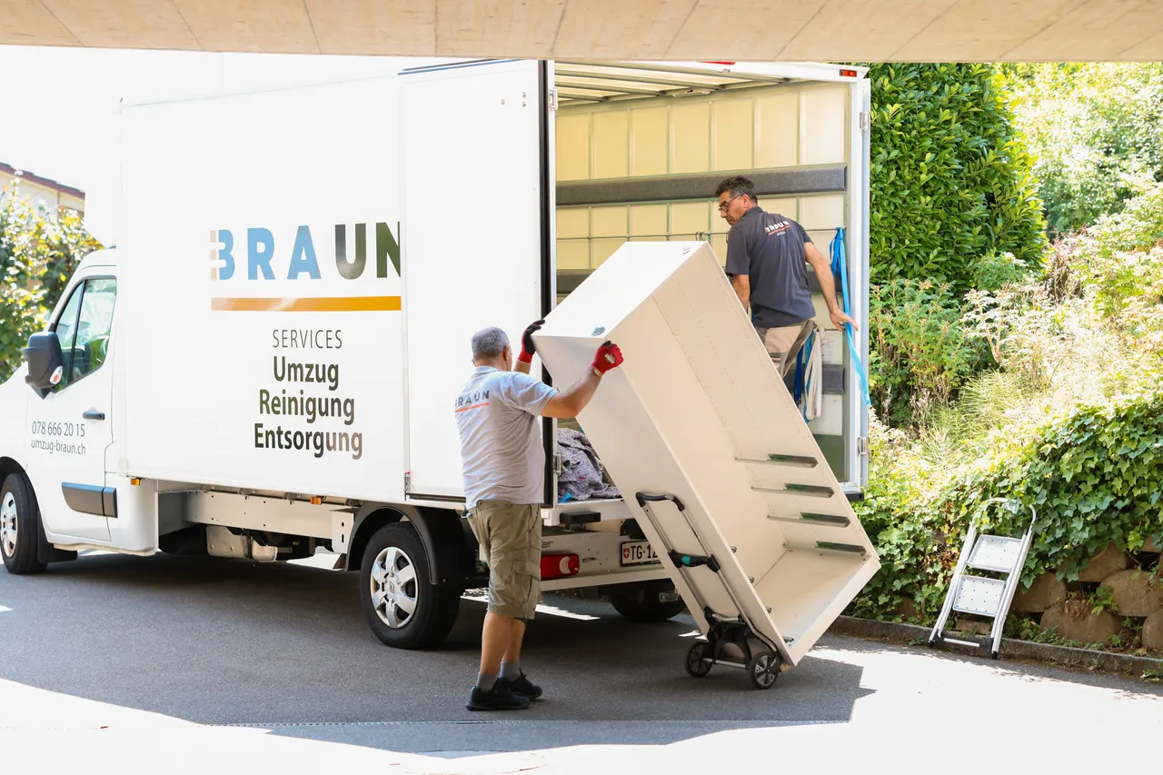 Mitarbeiter schiebt einen weissen Schrank auf der Sackkarre zum offenen Braun-Lastwagen