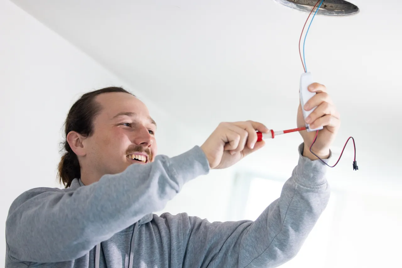 Junger Elektriker montiert lachend einen LED-Treiber an der Decke