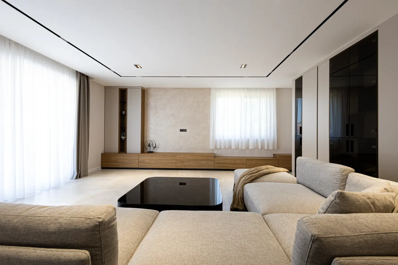 Heller Wohnraum mit Nussbaum-Lowboard, schwarzer Glasschrankwand und Lichtfuge in der Decke