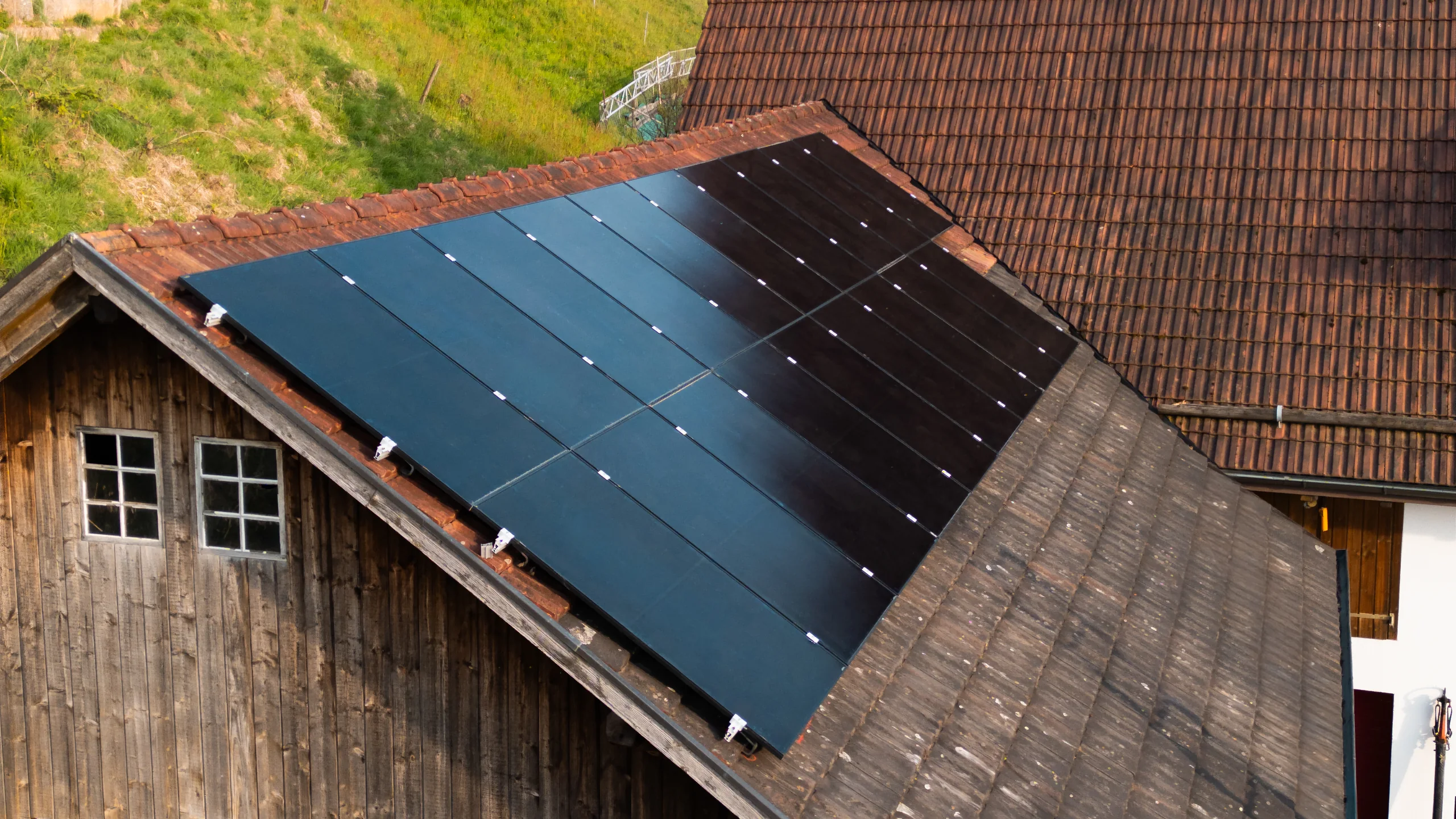 Drohnenaufnahme einer Photovoltaikanlage mit schwarzen Modulen auf dem Ziegeldach einer Holzscheune