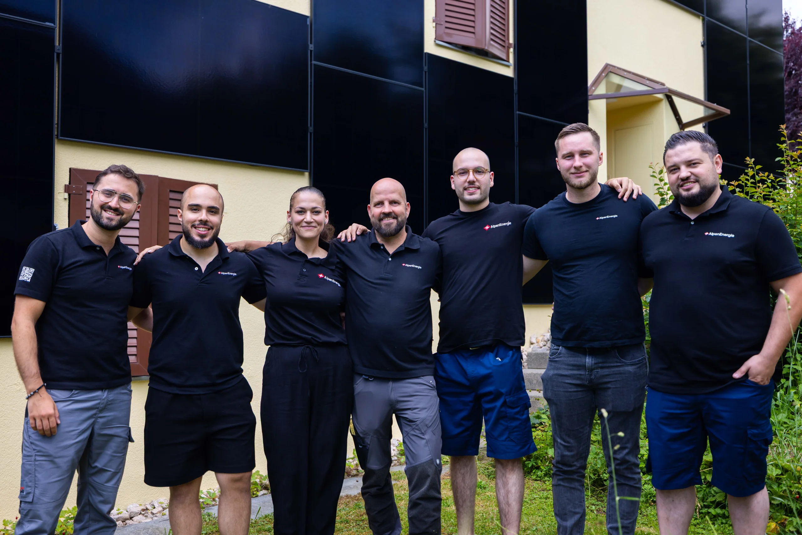 Das Team von AlpenEnergie vor einer Hausfassade mit schwarzen Solarmodulen
