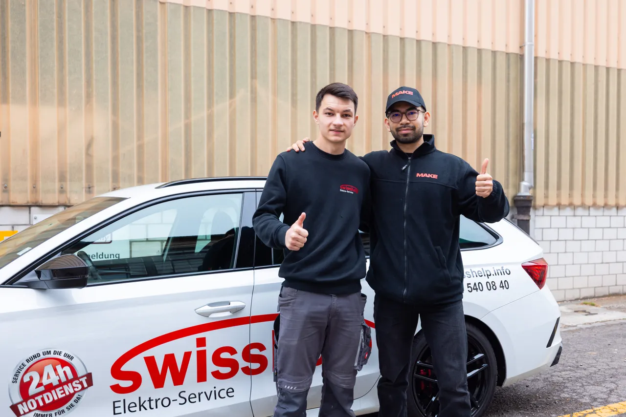 Ein Swisshelp-Mitarbeiter und der Fotograf von MAKE Arm in Arm vor einem beschrifteten Firmenwagen