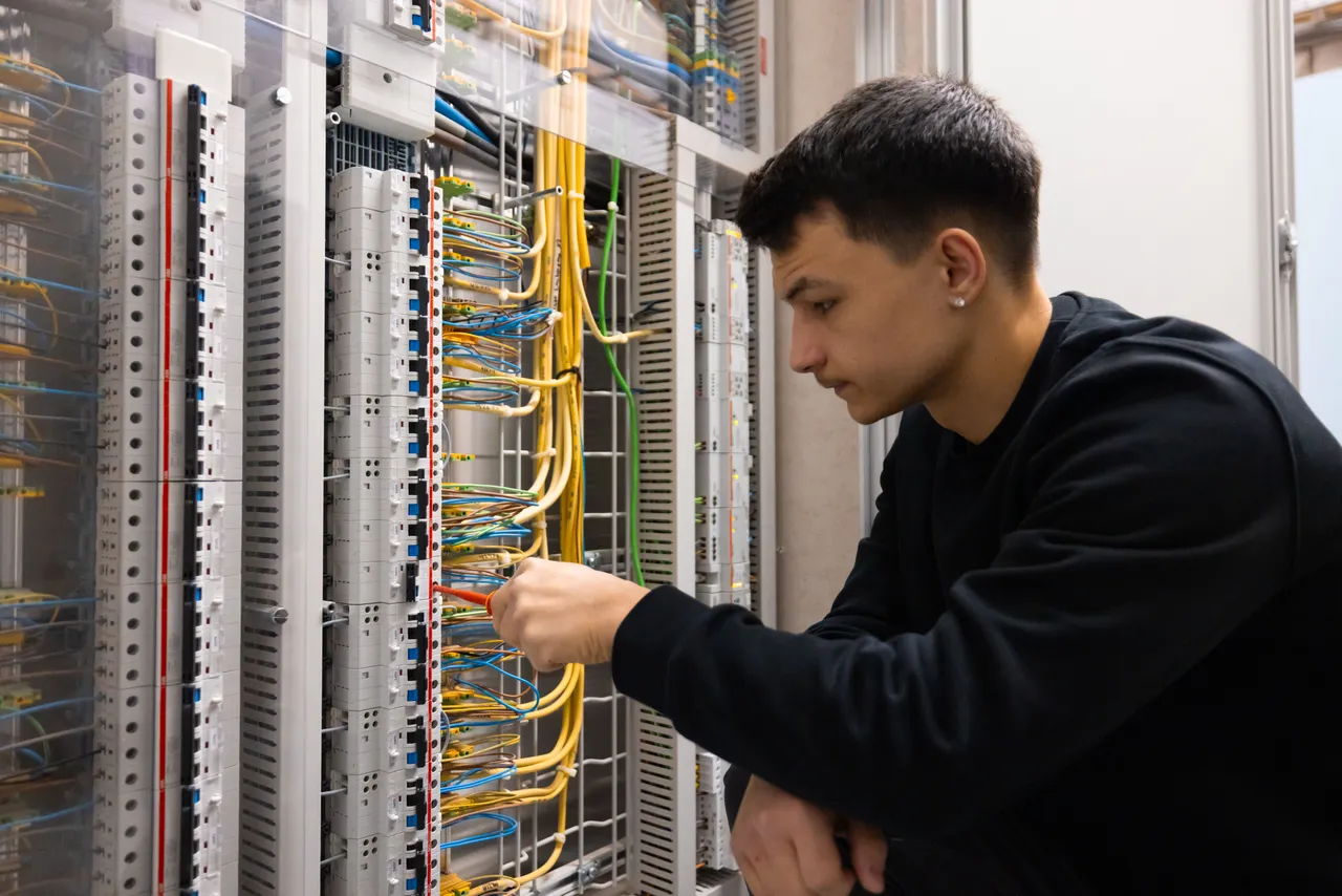 Junger Elektriker kniet konzentriert an einem grossen Verteiler mit gelben Leitungen