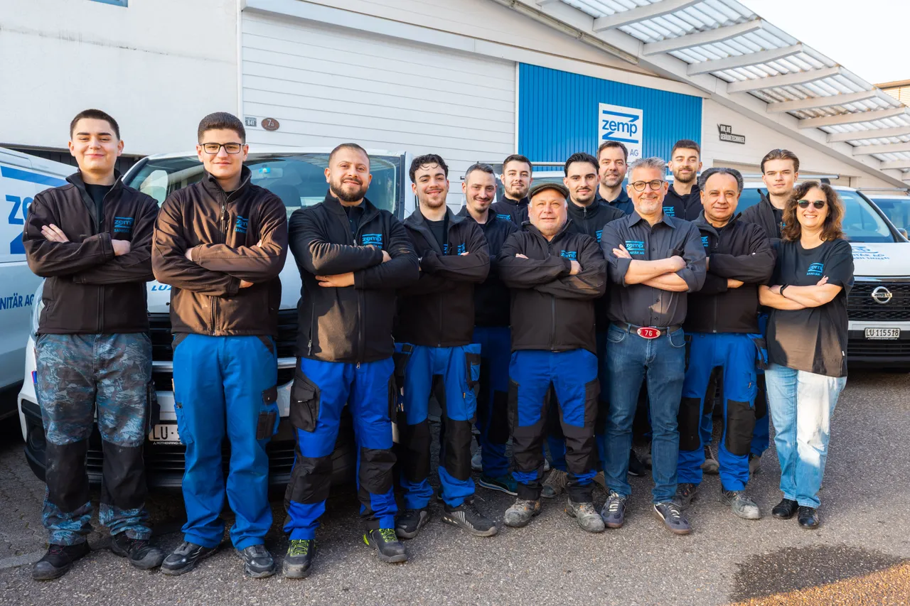 Das Team der Zemp Sanitär AG mit verschränkten Armen vor den Firmenfahrzeugen und dem Firmengebäude