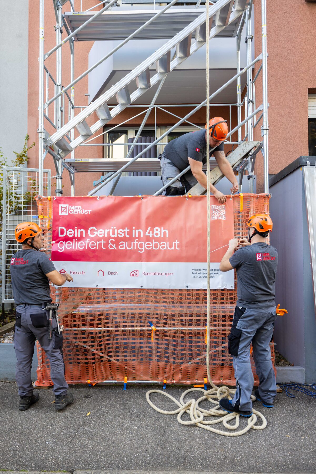 Gerüstbauer montieren ein Gerüst mit Werbeplane an einer Hausfassade