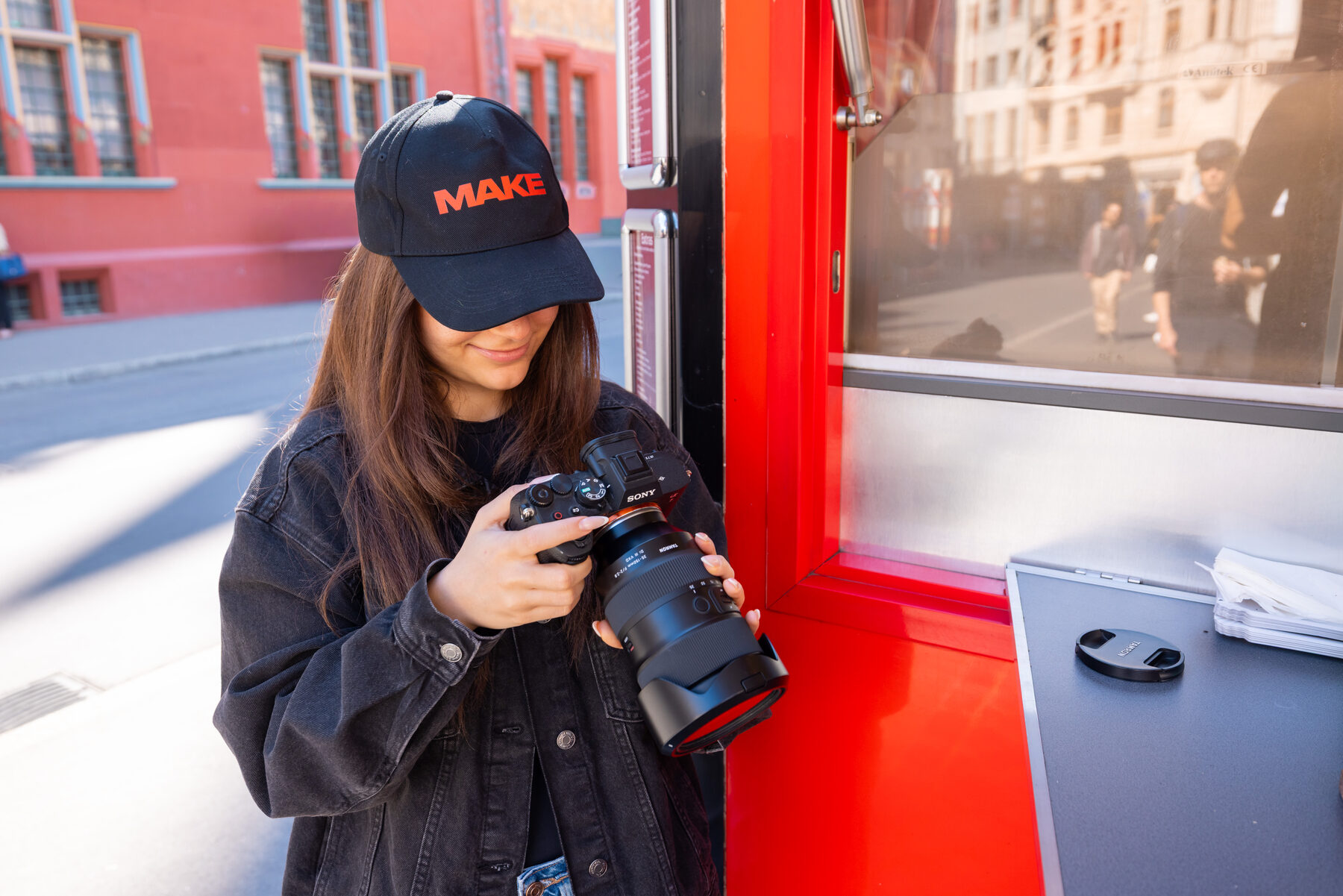 Fotografin mit roter Logo-Kappe prüft eine Aufnahme auf ihrer Kamera