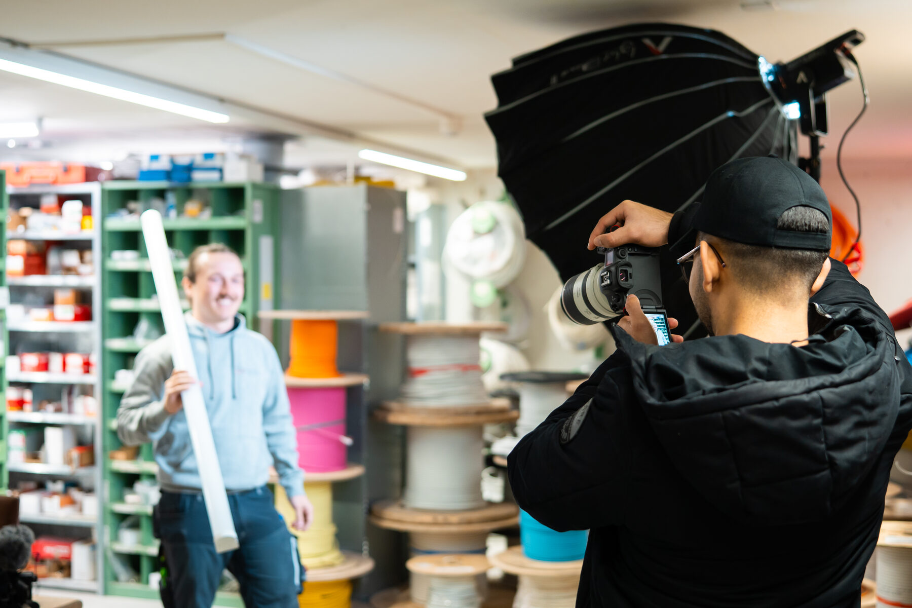 Fotograf mit Blitzschirm fotografiert einen Mitarbeiter in einem Lager mit Kabelrollen