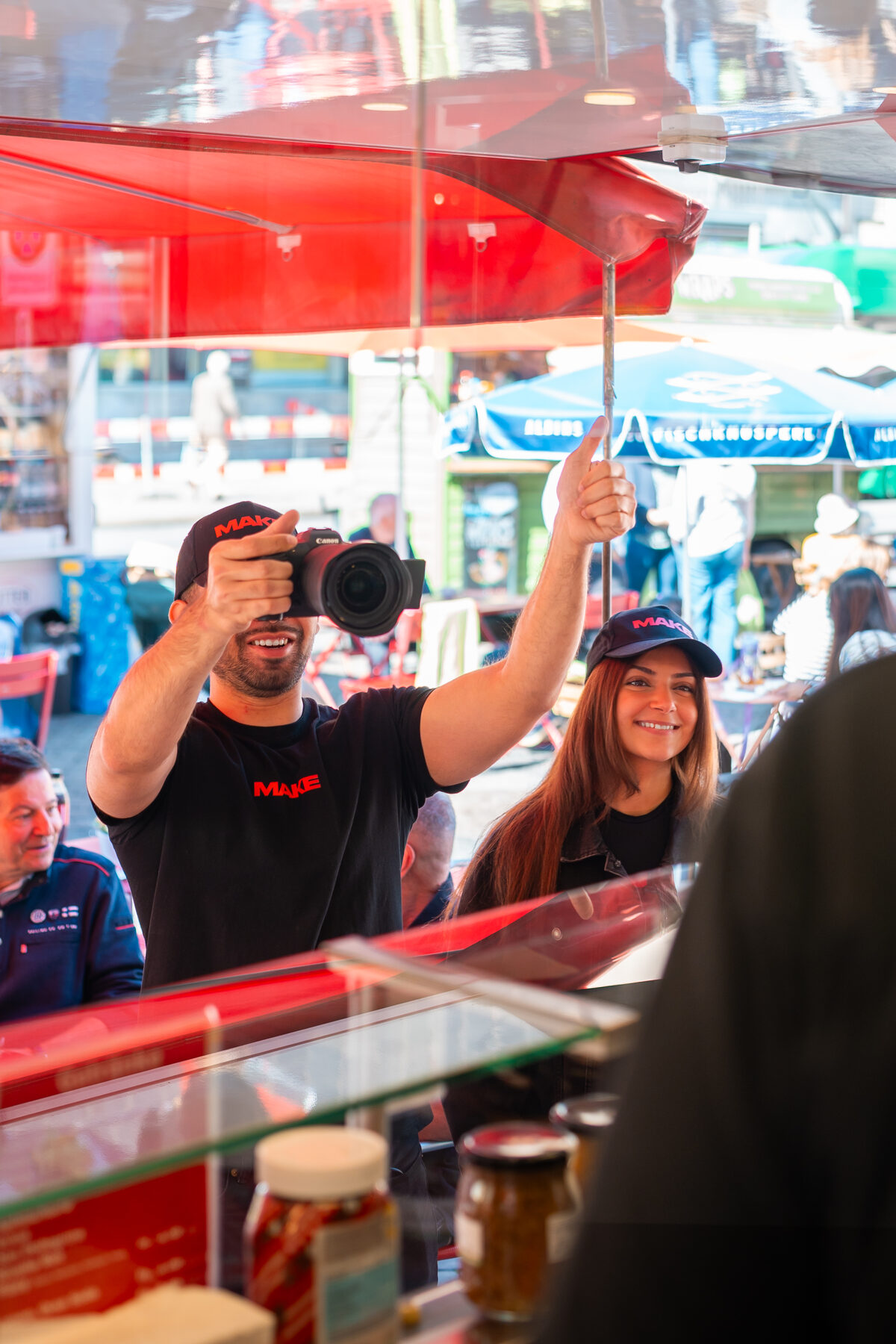 Zwei Fotografen mit Kameras unter einem roten Marktschirm